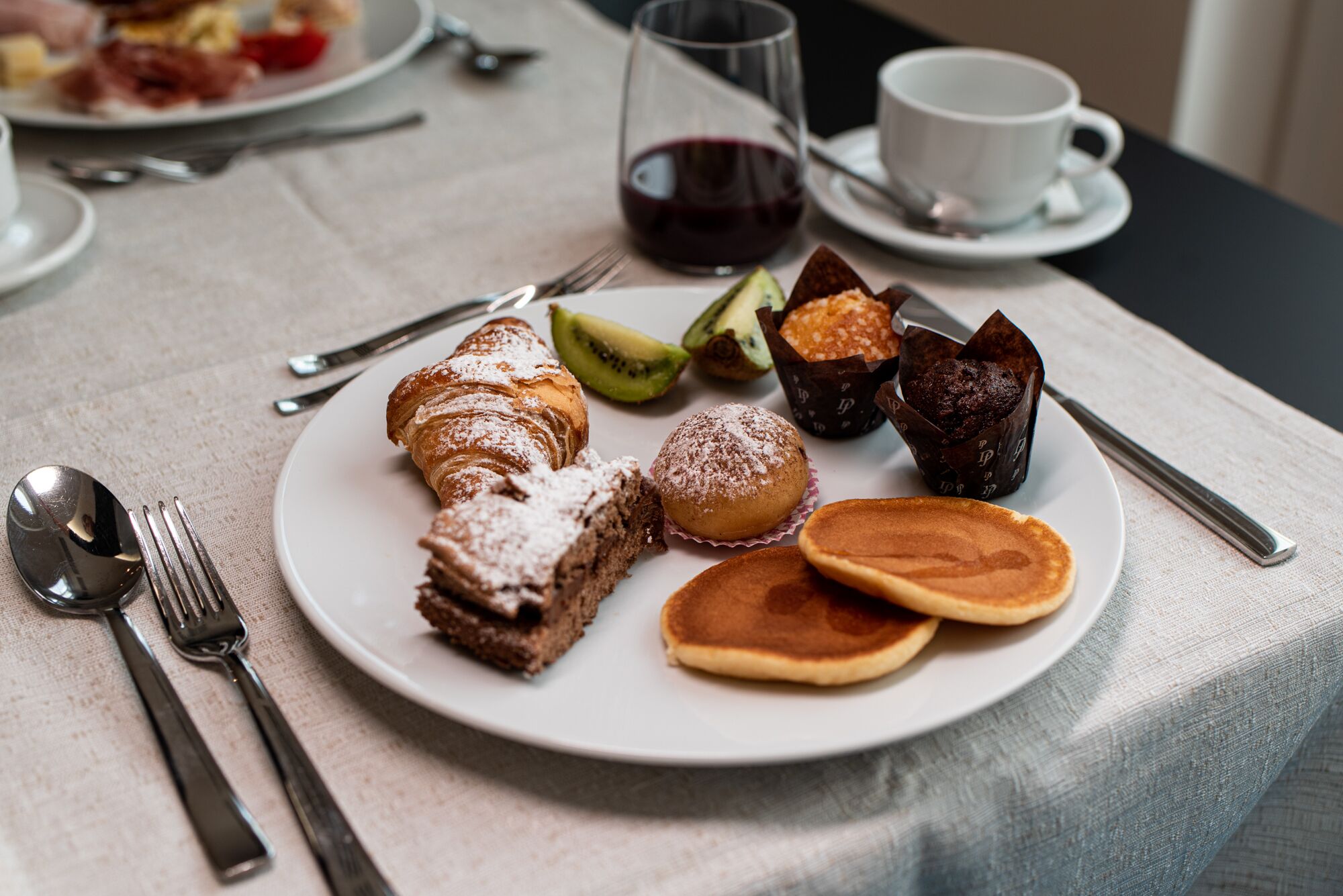 A breakfast plate with pastries, a glass of red wine, and a cup of coffee on a table.
