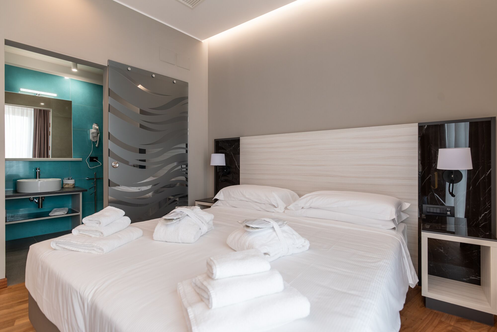 A modern hotel room with a large bed, a bathroom with a sink and mirror, and a decorative wall panel.