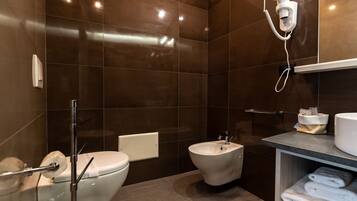 A modern bathroom with dark tiles, a toilet, bidet, and a towel rack.