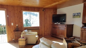 A cozy living room with wooden walls, a large window, a sofa, a television, and a wooden cabinet. - Wifi, Ground floor, view mountain, terrace, tv, ski locker, 94m², Le Grand Bornand (Le Grand-Bornand)
