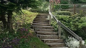 A wooden staircase surrounded by lush greenery and flowering plants. - Wifi, Ground floor, view mountain, terrace, tv, ski locker, 94m², Le Grand Bornand (Le Grand-Bornand)