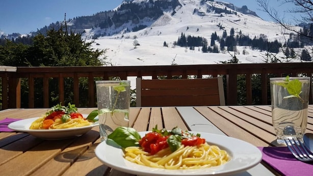 Two plates of pasta with vegetables on a wooden table with a mountain view in the background. - Wifi, Ground floor, view mountain, terrace, tv, ski locker, 94m², Le Grand Bornand (Le Grand-Bornand)