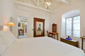A bedroom with a large bed, a desk with a mirror, a lamp, and a window with blinds.