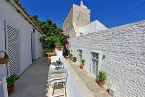 A narrow alleyway with white stone buildings, a small table with chairs, and potted plants.