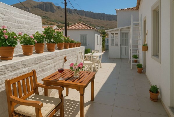A patio with a wooden table and chairs, surrounded by potted plants and a white wall.