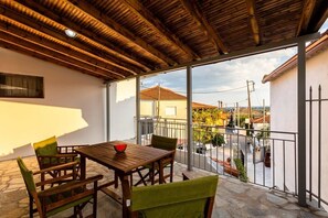 A balcony with a wooden table and chairs, a view of the neighborhood, and a tiled floor.