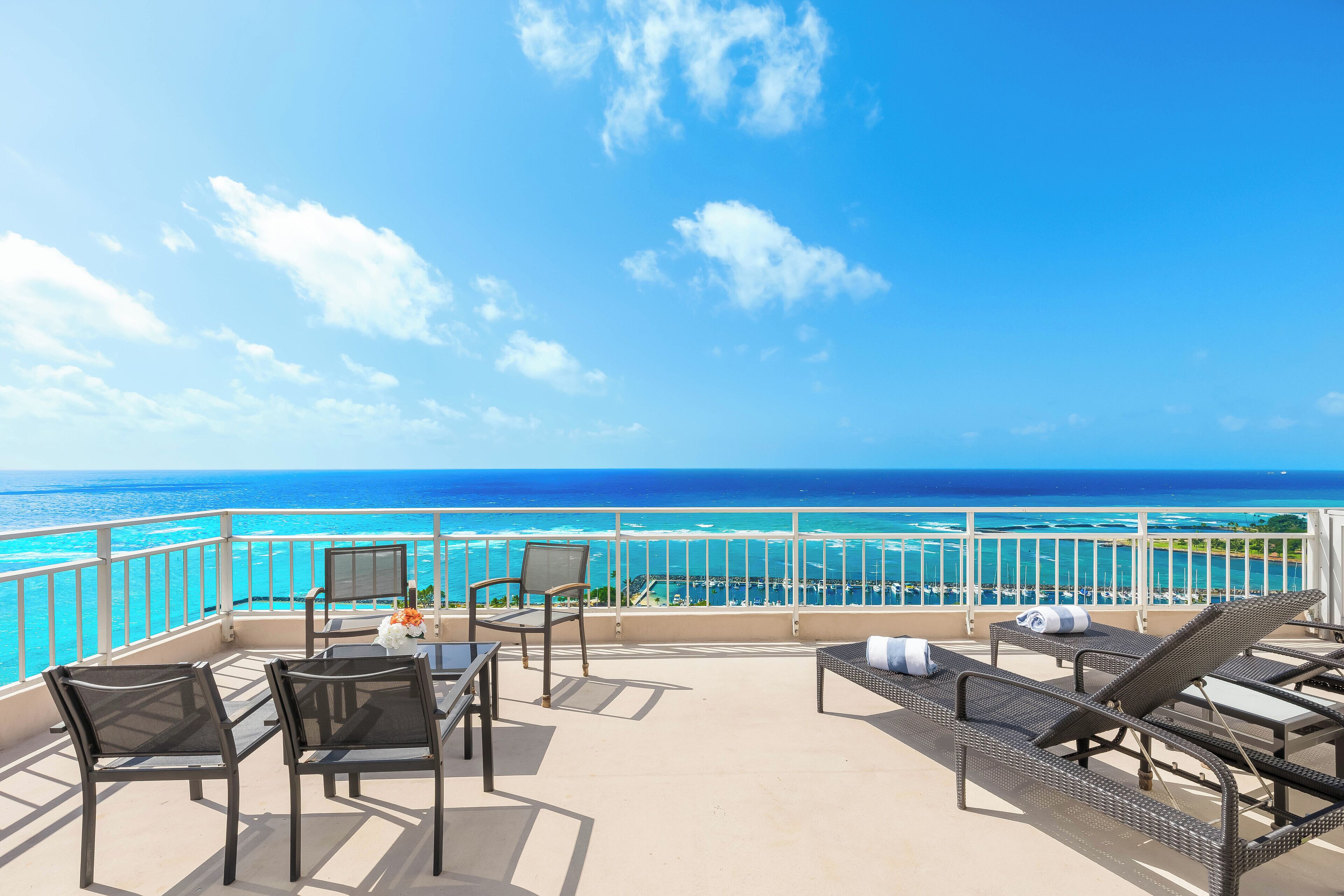 A balcony with a view of the ocean, furnished with chairs and a table, and a railing.