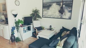 Un salon moderne avec un canapé d’angle gris foncé, une table basse blanche et un grand tableau représentant un phare accroché au mur.