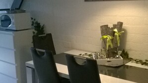 Une cuisine compacte avec un coin repas, agrémentée d’un luminaire suspendu moderne, d’une horloge et d’une petite plante posée sur le plan de travail.
