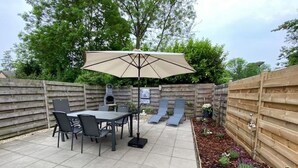 Une terrasse avec une table et des chaises, un barbecue et un espace salon abrité.