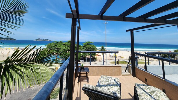 Ein Balkon mit Blick auf den Strand, Sitzgelegenheiten im Freien und einem klaren, blauen Himmel.