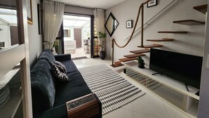 Ein modernes Wohnzimmer mit einer schwarzen Couch, einem Flachbildfernseher, einer Treppe mit Holzhäuschen und einem großen Fenster mit Vorhängen.