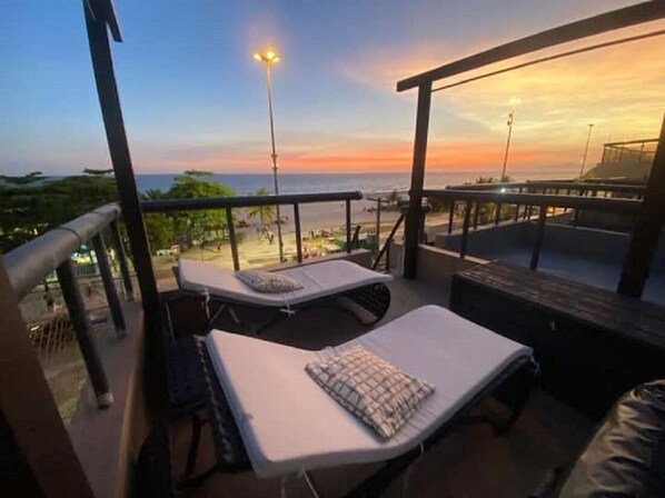 A rooftop lounge area with two sunbeds and a view of the beach at sunset. - AP Pepê Jacuzzi/solário (Rio de Janeiro)