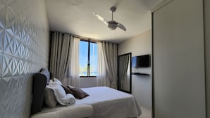 Ein modernes Hotelzimmer mit Bett, Deckenventilator, Wand-Fernseher und einem Fenster mit Vorhängen.