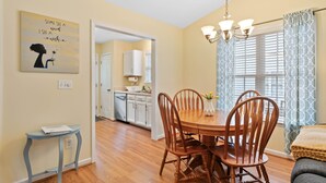 A dining area with a wooden table and chairs, a chandelier, and a painting on the wall.
