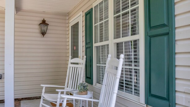 A porch with two white rocking chairs, a small table with a plant, and a wall-mounted lantern.