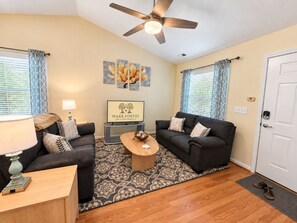 A living room with two sofas, a coffee table, a lamp, a ceiling fan, and artwork on the wall. - *Walk to Downtown * Fenced Yard (Wake Forest)