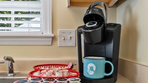 A coffee maker with a mug, a basket of coffee pods, and a tray of coffee cups.