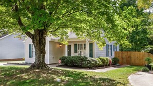 A single-story house with a front porch, a large tree, and a wooden fence.