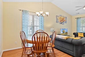 A dining area with a round wooden table and chairs, a chandelier, and a sofa with a throw blanket. - *Walk to Downtown * Fenced Yard (Wake Forest)