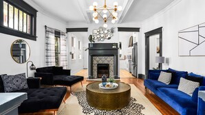 A modern living room with a fireplace, black and blue sofas, a round coffee table, and a chandelier. - Modern Midtown Getaway - Luxury and Chic (Atlanta)