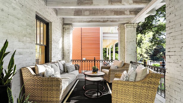 A covered outdoor seating area with wicker furniture, a round table, and a black rug. - Modern Midtown Getaway - Luxury and Chic (Atlanta)
