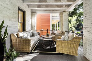 A covered outdoor seating area with wicker furniture, a round table, and a black rug. - Modern Midtown Getaway - Luxury and Chic (Atlanta)