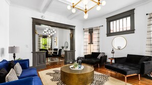 A modern living room with a blue sofa, black armchair, and a round coffee table. There is a large mirror, a chandelier, and a window with curtains. - Modern Midtown Getaway - Luxury and Chic (Atlanta)