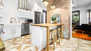 A modern kitchen with a central island, white cabinetry, stainless steel appliances, and a brick accent wall. - Modern Midtown Getaway - Luxury and Chic (Atlanta)