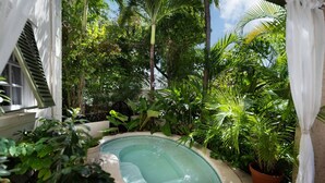 En privat pool omgivet af frodige tropiske planter og en hvid bygning med et vindue og skodder.