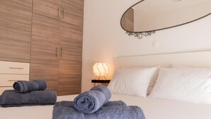 A neatly made bed with white linens and rolled gray towels. There is a bedside lamp with a geometric light fixture. A large mirror with a curved frame is mounted on the wall above the bed. - GTD31504 - Art room of Athens - Luna (Palaio Faliro)