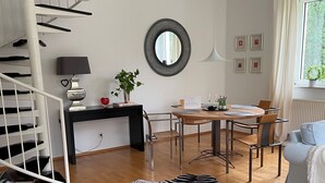 Uma sala de estar moderna com uma escada em espiral, uma área de jantar com mesa redonda e vista para o verde lá fora.