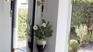 Um interior moderno com um espelho grande, um console com um vaso de flores e vista para um jardim através de uma porta de vidro.