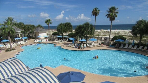 A pool area with lounge chairs and umbrellas, a beach in the background, and palm trees. - Beach Club D0302- Direct Gulf View - Beach - Pool - WIFI (Gulf Shores)