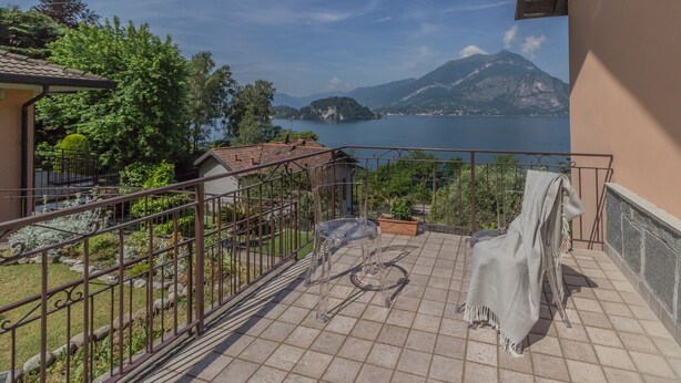 A terrace with a view of a lake and mountains, featuring a metal railing, a table, and a chair. - Varenna La Bomboniera (Varenna)