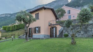 A two-story house with a stone staircase leading to the upper floor, surrounded by lush greenery and mountains in the background. - Varenna La Bomboniera (Varenna)
