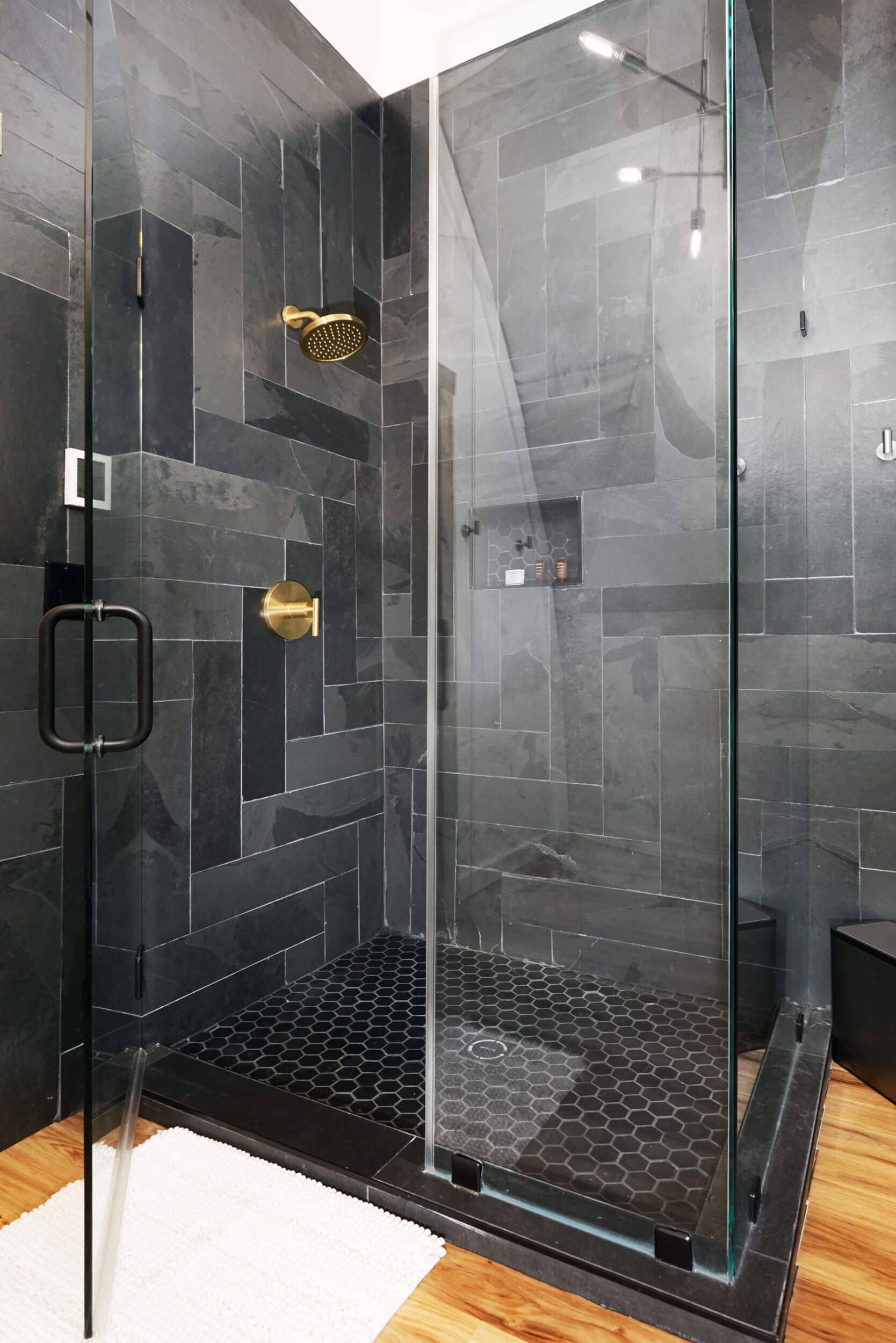 A glass-enclosed shower with a black tiled floor and a gold showerhead.