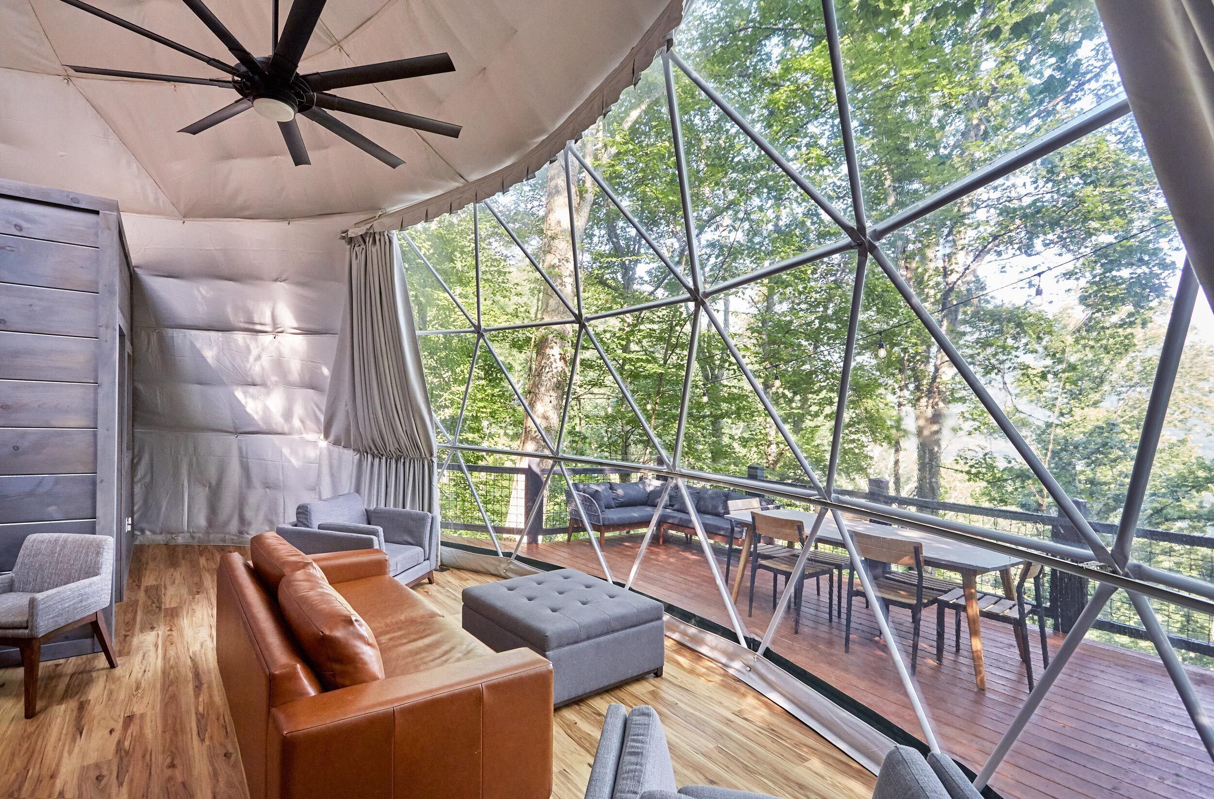 Ein großzügiges, modernes Interieur mit Holzboden, Ledersitzmöbeln und einem großen Fenster mit Blick auf den umliegenden Wald.