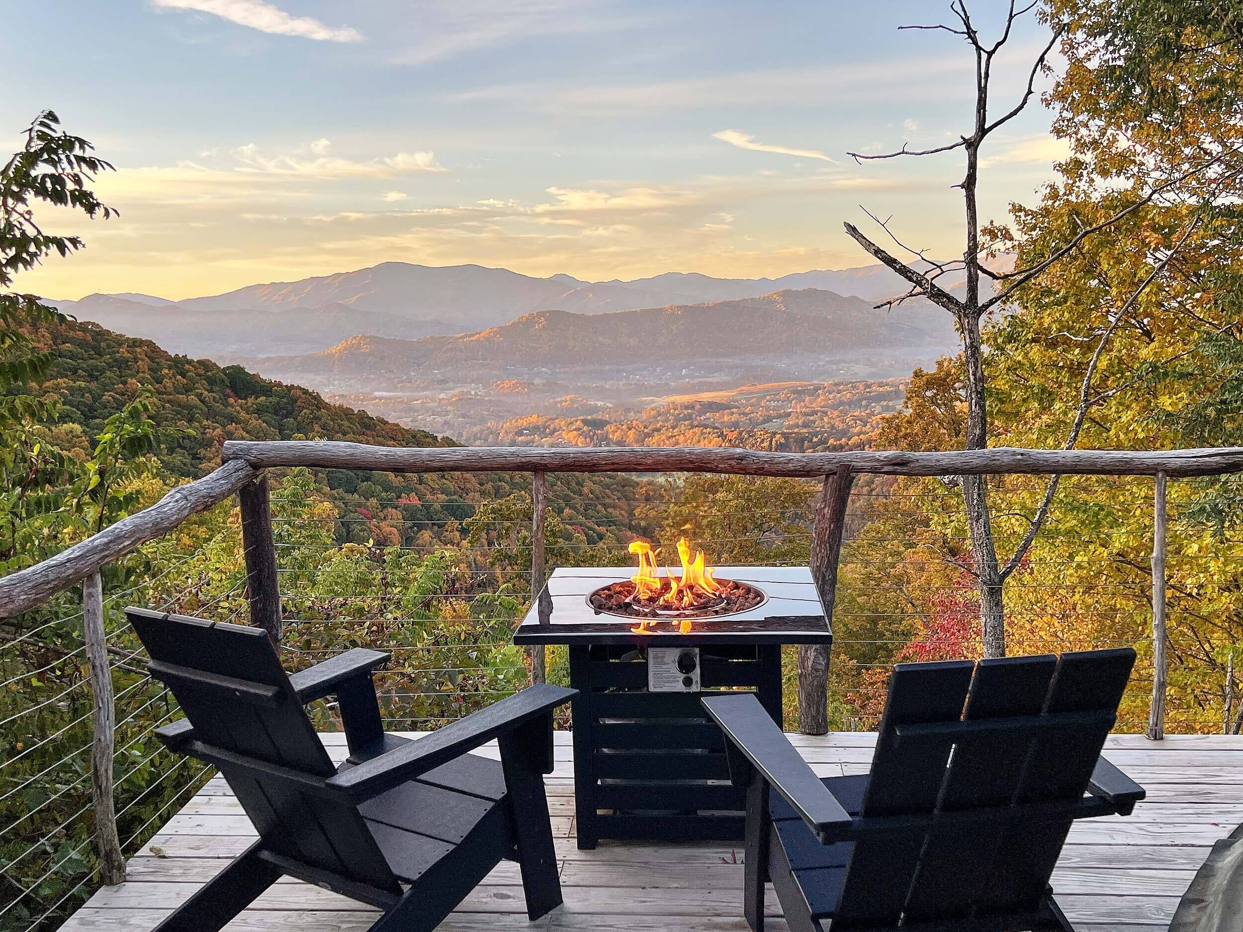 A deck with a fire pit and two chairs, overlooking a mountainous landscape.