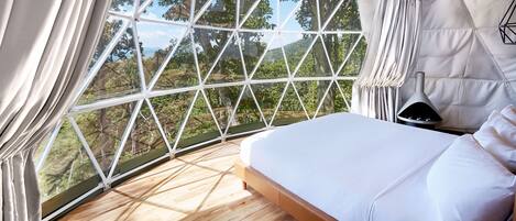 Un dormitorio con un ventanal grande, una cama y una mesita de noche.