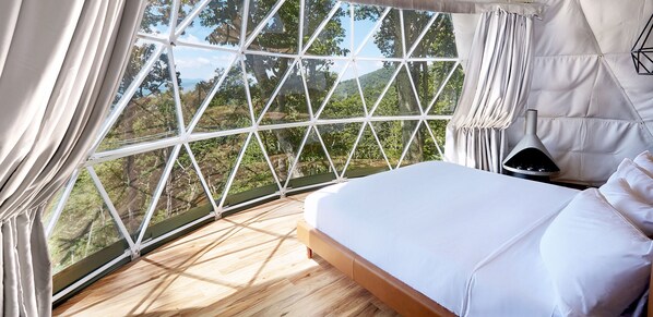 Un dormitorio con un ventanal grande, una cama y una mesita de noche.