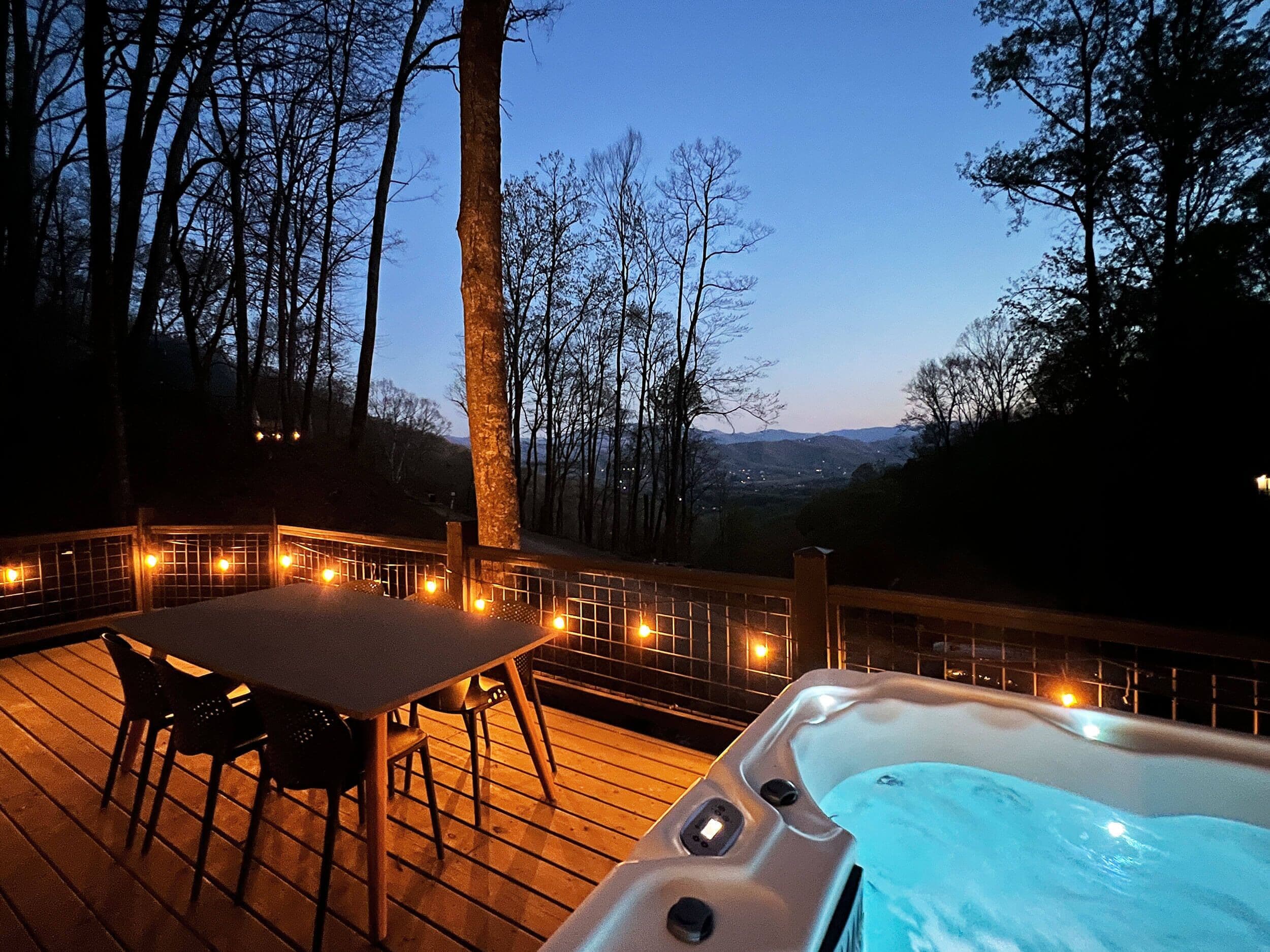A wooden deck with a hot tub, chairs, and string lights.