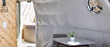 Una habitación con carpa, suelo de madera, una mesa con planta en maceta y un espejo redondo en la pared.