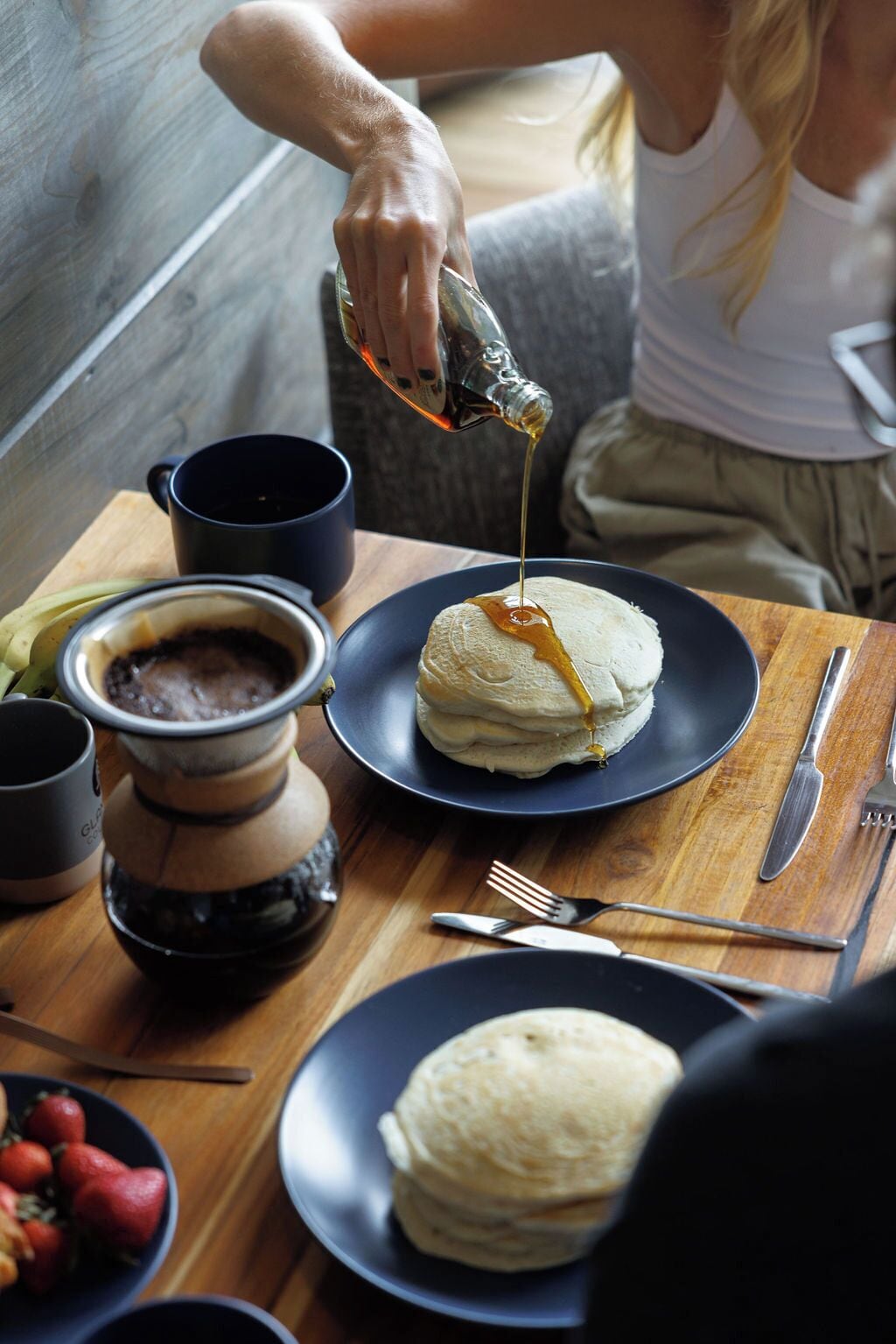 Une personne versant du sirop sur des crêpes dans une assiette.