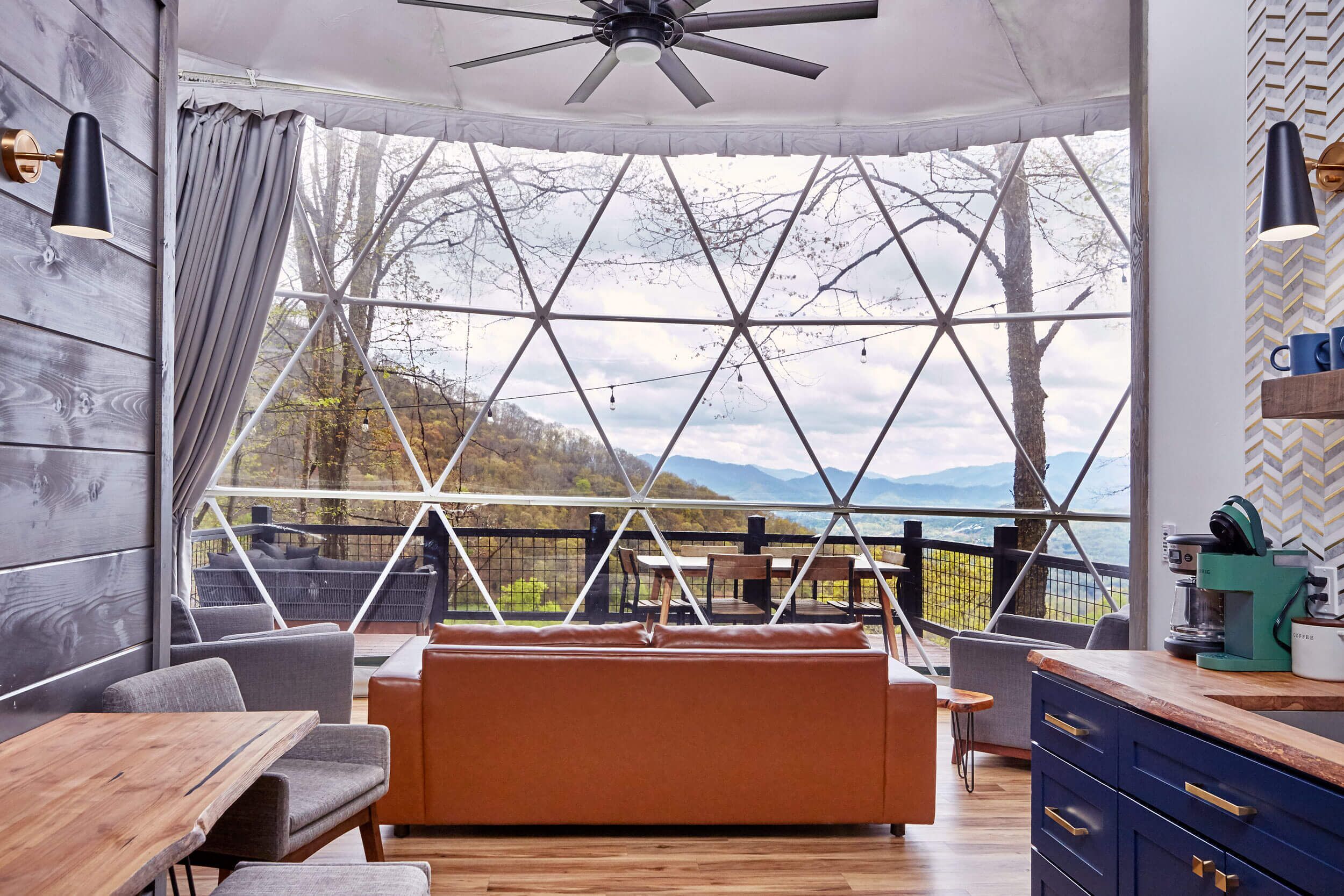 Um interior moderno com uma mesa de madeira, assentos acolchoados, uma área de cozinha e uma janela grande com vista para o exterior.