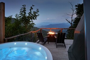 A hot tub on a wooden deck with a fire table and chairs, overlooking a mountainous landscape. - The Glamping Collective (Clyde)