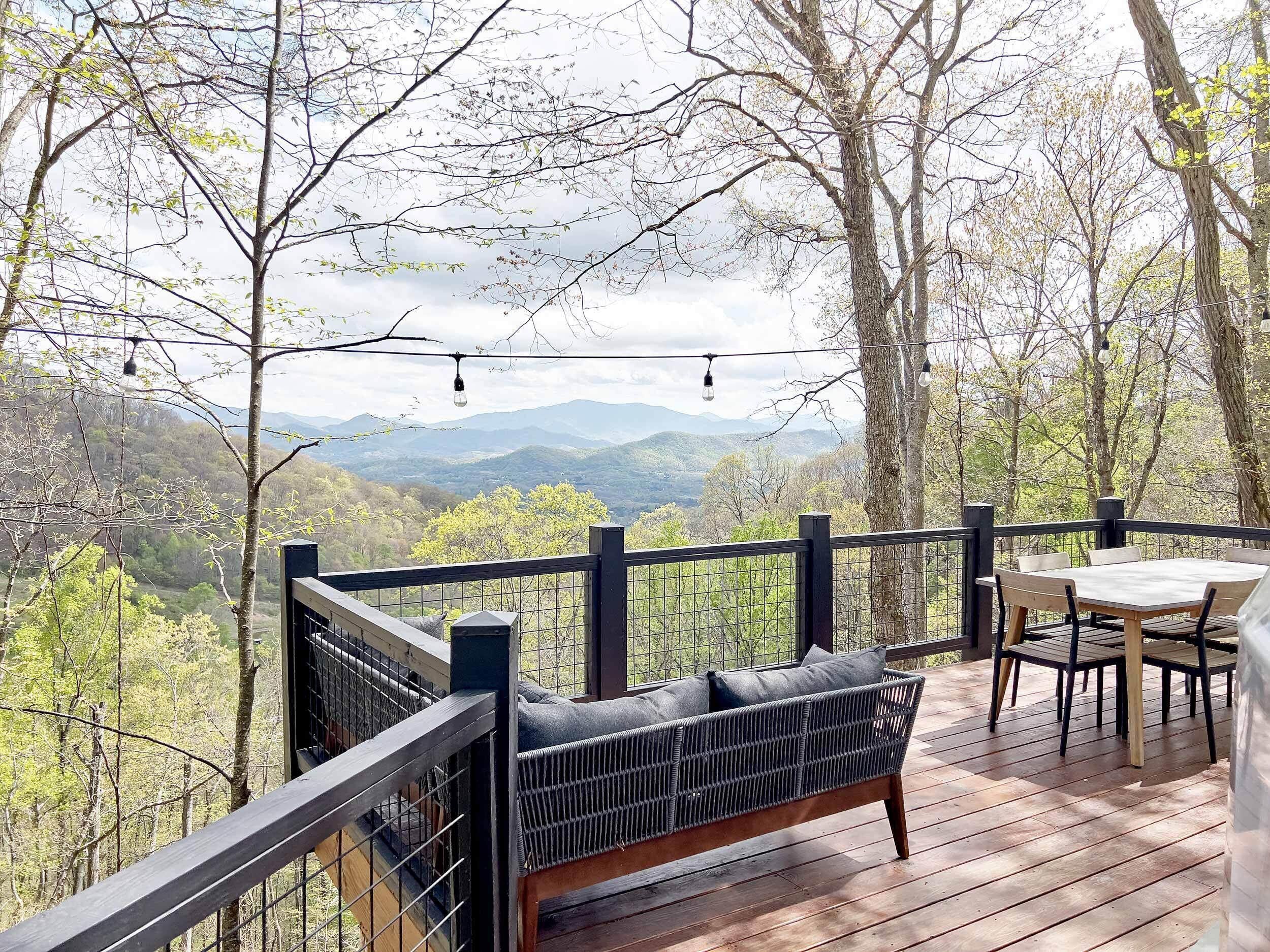 A wooden deck with a black metal railing, a wicker sofa, and a table with chairs.