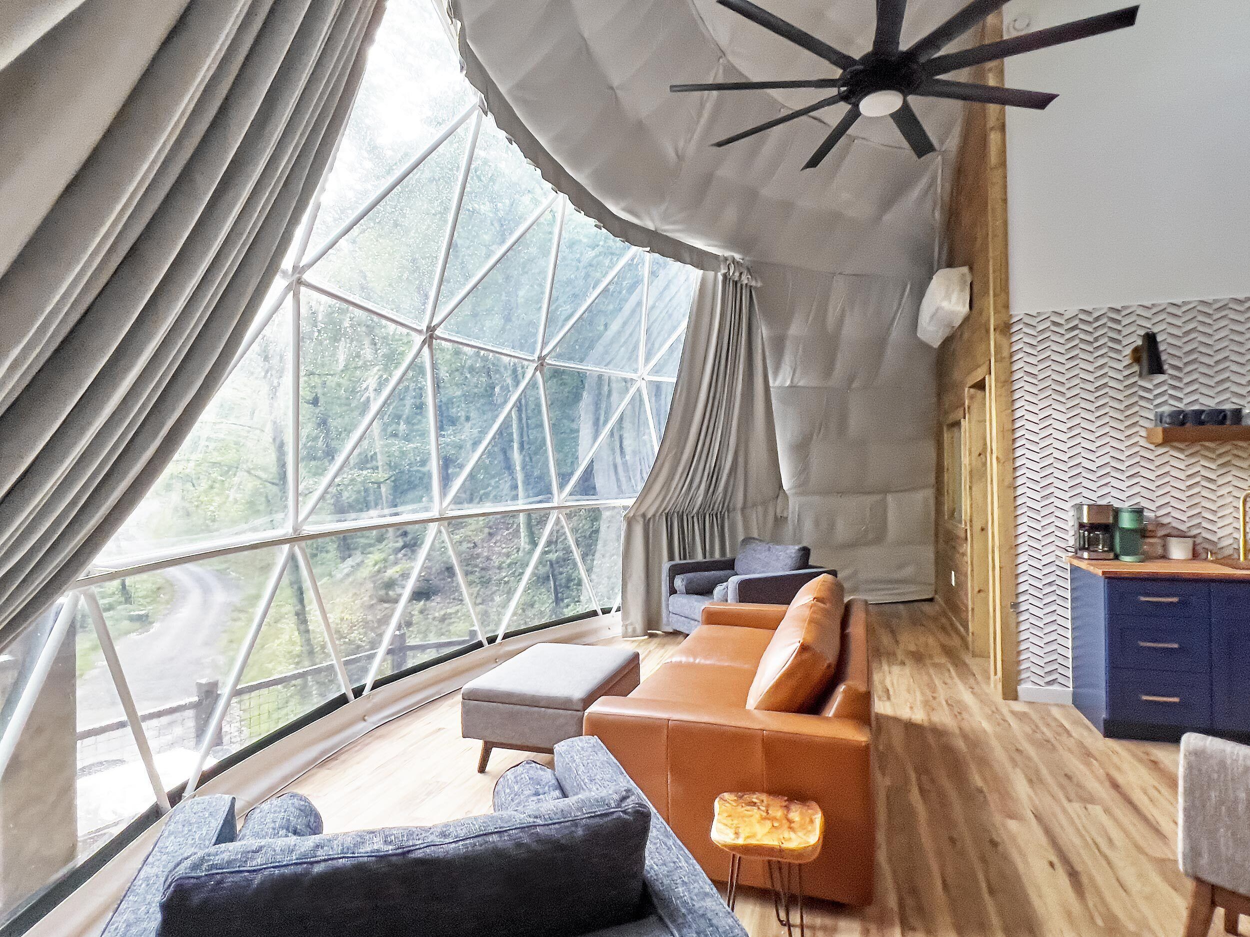 Een modern interieur met een groot raam, een plafondventilator, een bank en een kleine kitchenette.