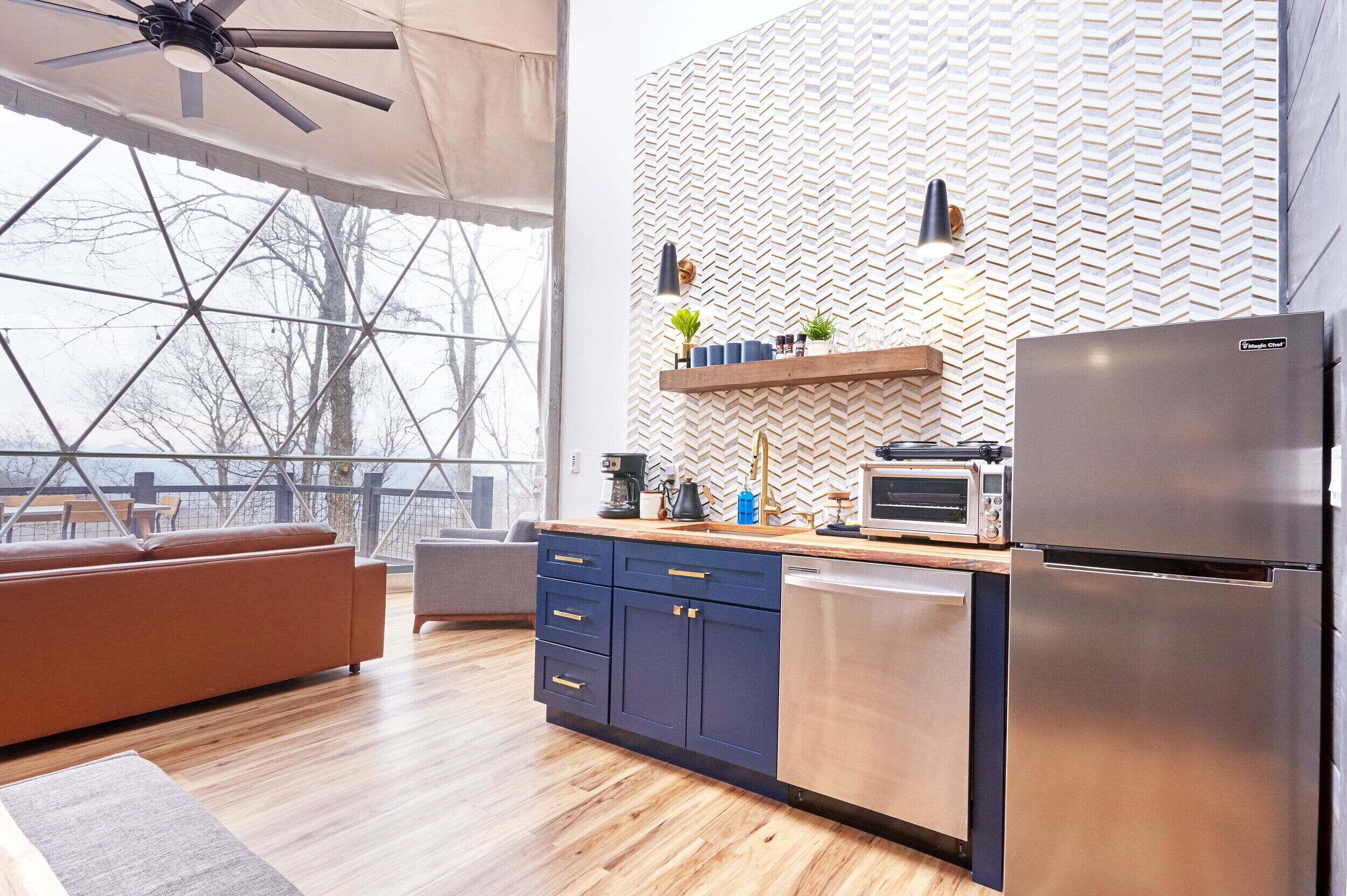 A modern kitchen with a herringbone-patterned backsplash, a built-in oven, and a stainless steel refrigerator.