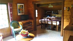 A wooden interior with a dining area, a kitchen visible through an open doorway, and a television on a wooden stand.